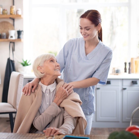 A caregiver standing with an older woman in a bright kitchen, both smiling